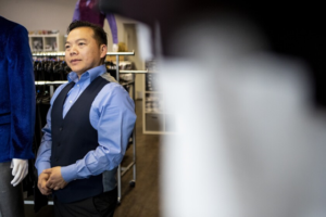 Sean Yang, owner of the store, stands wearing a blue shirt with vest.