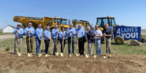 Members of the Highway 23 Highway Coalition wear matching blue polos while holding shovels. They are standing in front of a dump truck and a sign that says "4 Lanes 4 You"
