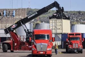 A truck and crane load a shipping container on a ship in the Duluth port