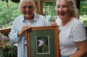 Two women pose with a framed picture of a showy lady slipper