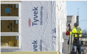 Men in hard hats put up insulation at a construction site for a housing until