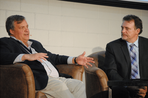 Two men sit on a stage talking